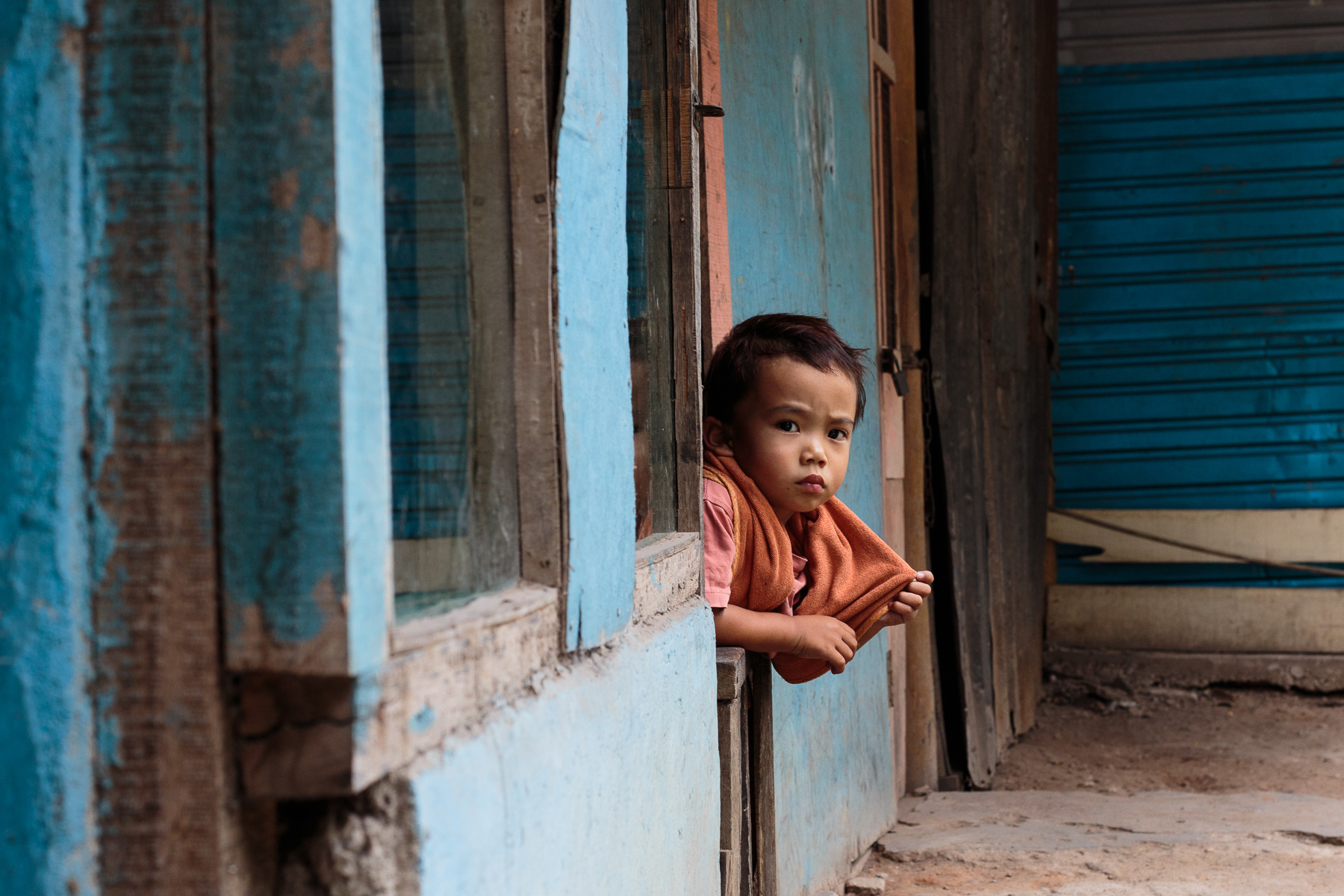 Indonesia - Child in red takes a peek from a door with a blue wall